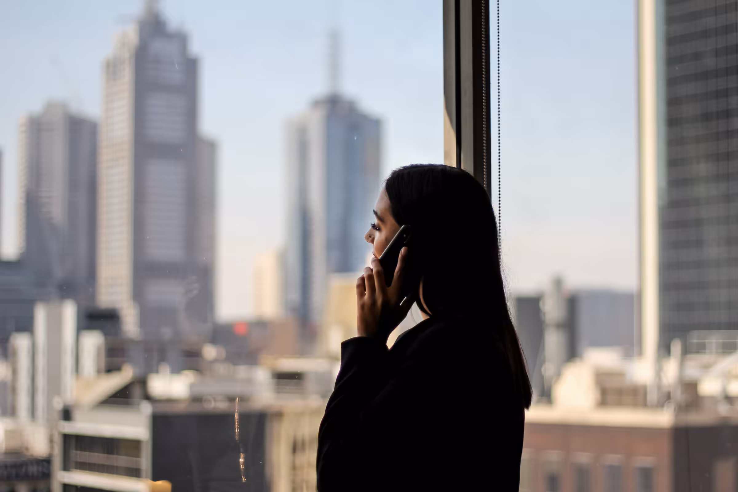 A lawyer taking a call at a window, the city skyline behind her